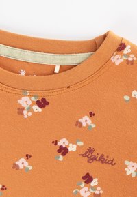 Kurzärmliges, rost-orange Baumwoll-T-Shirt mit floralen Mustern in Rosa, Weiß und Grün. Mit rundem Ausschnitt und gesticktem Logo.