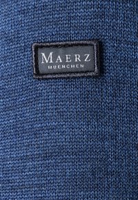 Tessuto lavorato a maglia blu navy con un motivo testurizzato. Presenta un'etichetta nera con la scritta "Maerz Muenchen" in lettere bianche cucita sopra.
