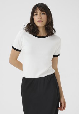 T-shirt blanc à manches courtes avec un col et des poignets côtelés contrastants noirs, fabriqué en tissu lisse. Porté avec une jupe noire.