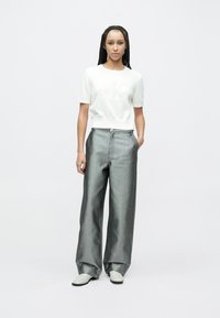 Pulover alb cu mâneci scurte și logo embosat, asortat cu pantaloni gri din denim, talie înaltă și cu picioare largi. Modelul poartă pantofi de culoare deschisă.