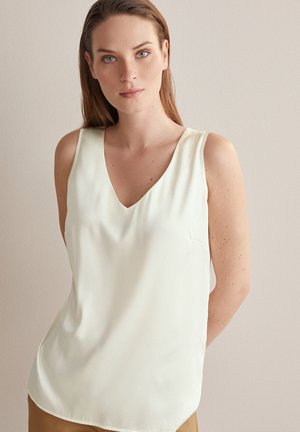 Blouse sans manches à décolleté en V en tissu crème clair. Texture lisse avec une légère brillance, dotée d'une poche latérale et d'une coupe décontractée.