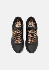 Schwarze Sportschuhe mit Leopardenmuster Schnürsenkeln, glattem Außenmaterial und Perforierungen. Mit Snoop Dogg-Branding an den Seiten und auf den Innensohlen.