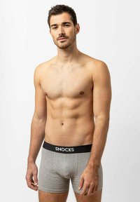 Grijze boxer shorts met zwarte elastieken tailleband met het logo "SNOCKS". Zachte stof en slank ontwerp. Model staat tegen een witte achtergrond.