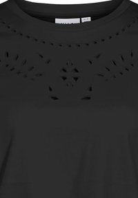 Camiseta negra con cuello redondo y patrones decorativos recortados en el pecho, hecha de una tela suave con un acabado mate.