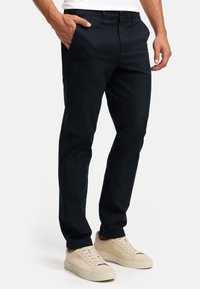 Marineblaue Chinos aus einem glatten Baumwollgemisch. Mit seitlichen Taschen und einer taillierten Passform, kombiniert mit hellbeigen Sneakers.