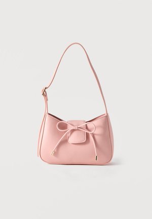 Petit sac bandoulière rose pastel avec sangle réglable et détail nœud à l'avant avec extrémités dorées sur un fond uni.