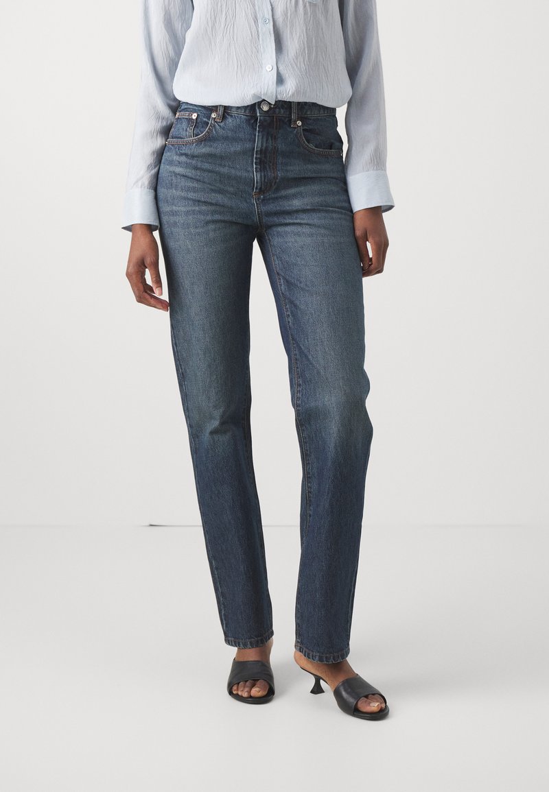 Hoge taille blauwe denim jeans met een rechte pijp, voorzien van subtiele stikseldetails en een vijf-pocket ontwerp, gecombineerd met een lichtblauw shirt.
