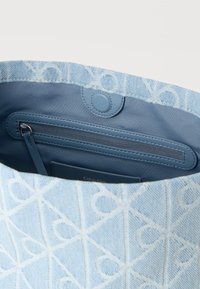 Τσάντα ώμου ανοιχτού γαλάζιου χρώματος με υφασμένο εξωτερικό μέρος που φέρει λευκά γεωμετρικά σχέδια, εσωτερική τσέπη με φερμουάρ και κούμπωμα με κουμπί.