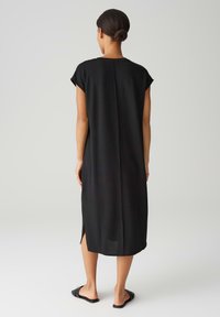 Zwarte, knielange jurk met korte kapmouwen, een rechte silhoeet en zijsplitten. Gemaakt van zachte, lichte stof.