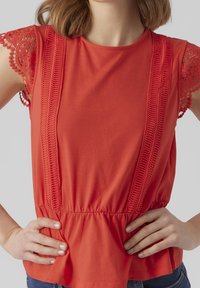 Punainen lyhythihainen toppi, jossa on virkattu pitsiakkenttiä hihoissa ja teksturoitu peplum-vyötärö. Pehmeä kangas, jossa on rento istuvuus.