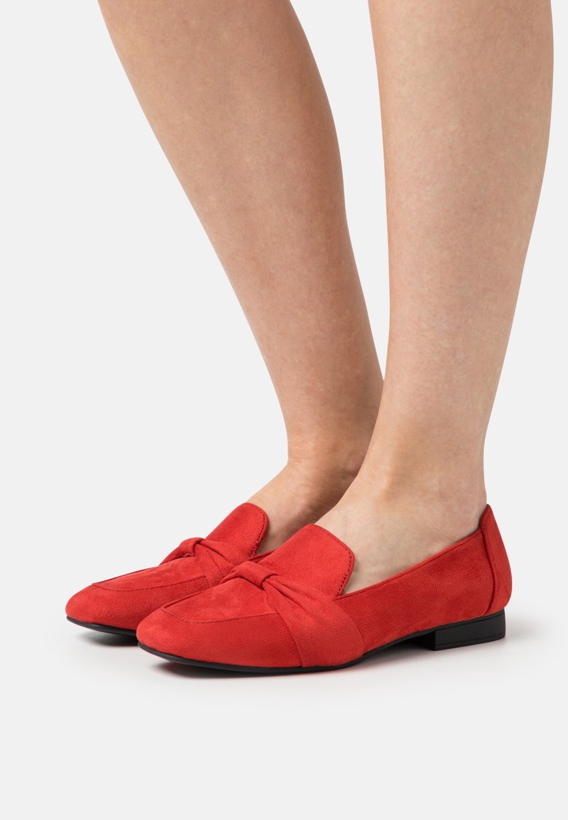 Ballerines en daim rouge avec un détail de nœud sur le dessus, présentant un bout arrondi et un petit talon noir. Texture douce, design épuré.