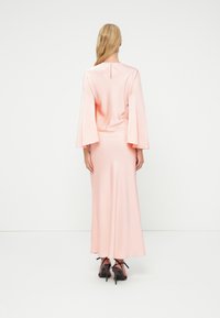 Ρόμπα ροζ με μακριά μανίκια, λεία υφή, φουσκωτά μανίκια και λεπτομέρεια κλειδαρότρυπας στο πίσω μέρος, συνδυασμένη με μαύρες ψηλοτάκουνες γόβες.