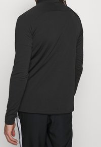 Schwarzes Langarm-Athletikshirt aus glattem, dehnbarem Material. Verfügt über einen hohen Kragen und ein enganliegendes Design mit minimalen Nähten auf der Rückseite.