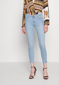 Ljusblåa skinny jeans med hög midja, tillverkade av denim. Har minimal sömnad och rå fåll vid ankeln, i kombination med svarta klackar.