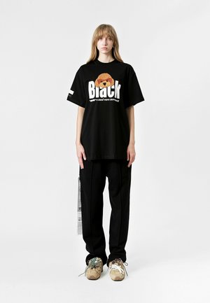 Camiseta negra de gran tamaño con estampado gráfico y texto en blanco. Combinada con pantalones sueltos negros y zapatillas chunky en tonos beige y verde.