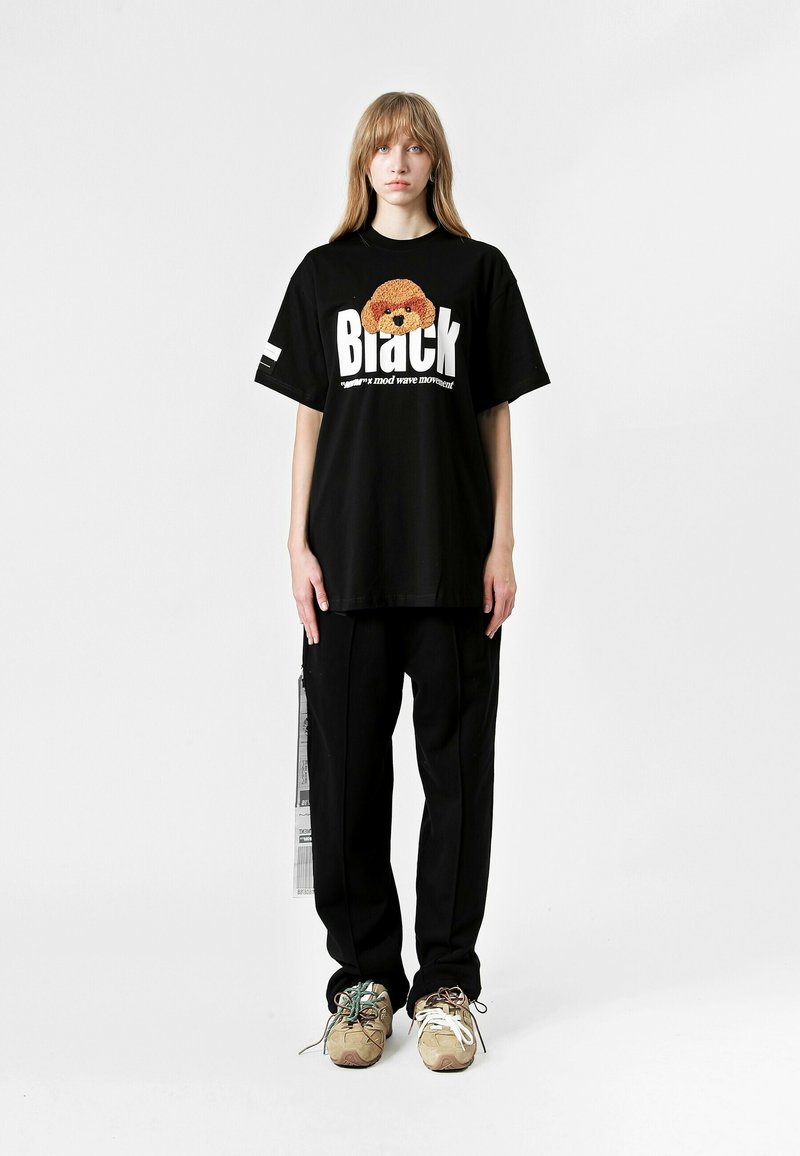 Camiseta negra de gran tamaño con estampado gráfico y texto en blanco. Combinada con pantalones sueltos negros y zapatillas chunky en tonos beige y verde.