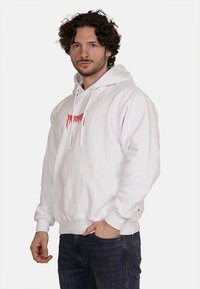 Hoodie bianco con tasca frontale, caratterizzato da testo grafico rosso sul petto e cordini. Realizzato in tessuto morbido, con polsini a costine.