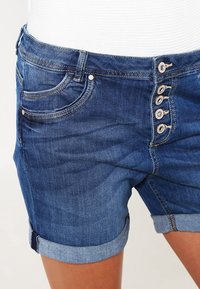 Jeansshorts i mörkblå med fem knappar fram, rullade fållar och sidofickor. Slät yta med sömnadsdetaljer.