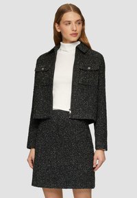 Schwarze, strukturierte, kurz geschnittene Jacke mit zwei vorderen Taschen, die sich mit einem Reißverschluss schließen lässt, kombiniert mit einem passenden Rock. Verfügt über ein minimalistisches Design und einen klassisch geschnittenen Kragen.