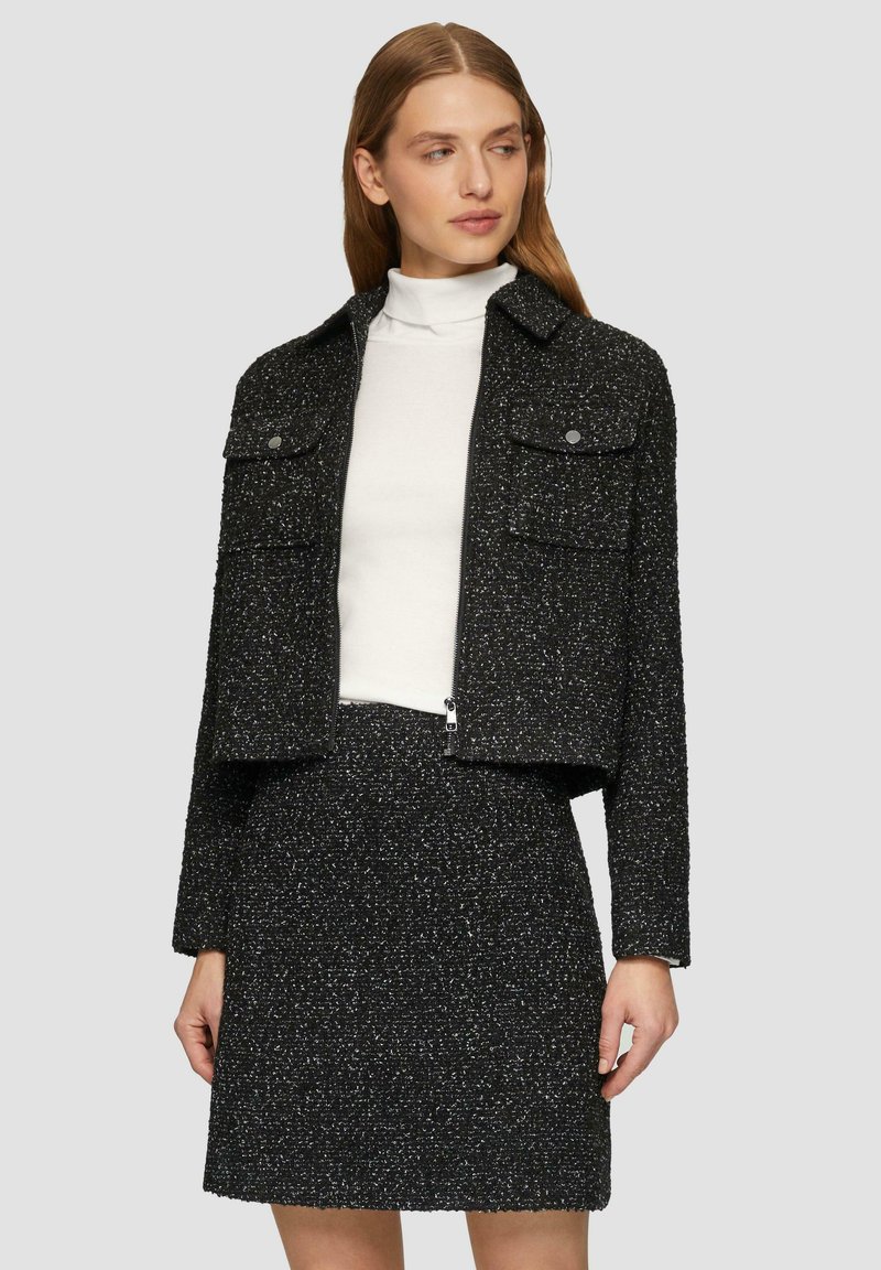 Schwarze, strukturierte, kurz geschnittene Jacke mit zwei vorderen Taschen, die sich mit einem Reißverschluss schließen lässt, kombiniert mit einem passenden Rock. Verfügt über ein minimalistisches Design und einen klassisch geschnittenen Kragen.