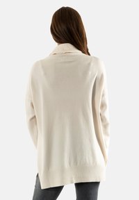 Suéter crema de gran tamaño con cuello alto, puños y dobladillo acanalados. Textura suave con un corte relajado, con aberturas laterales en la parte inferior.