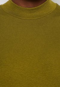 Sweter w kolorze oliwkowym z golfem, wykonany z materiału prążkowanego, z wysokim dekoltem i gładką teksturą. Zbliżenie ukazujące szczegóły materiału.