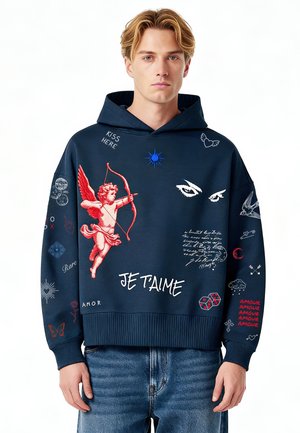 Giovane uomo che indossa una felpa con cappuccio blu navy con Cupido rosso, occhi bianchi, testo scritto a mano "Je t'aime", dadi e varie piccole illustrazioni grafiche.