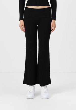 Sorte, ribbede strikkede flared bukser med høj talje, glat tekstur og bred ben design, parret med hvide sneakers.