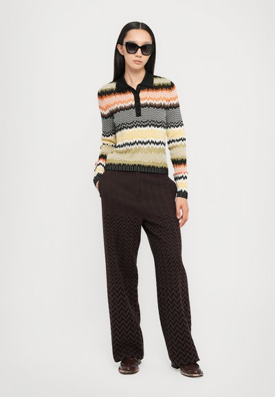 Pullover a maglia con motivo a zigzag multicolore, dotato di colletto nero e patta con bottoni. Paio di pantaloni a gamba larga a motivo chevron marrone scuro.