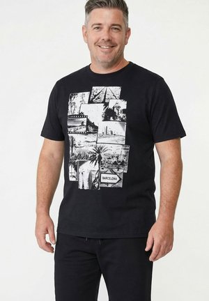 Uśmiechnięty mężczyzna w czarnej koszulce z czarno-białą kolażem scen z Barcelony, w tym z palmami i tablicą informacyjną.