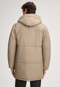 Beżowa pikowana kurtka z kapturem, z poziomymi szwami i prostym krojem. Tkanina wydaje się gładka o miękkiej fakturze.