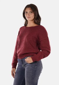 Maglione lavorato a maglia nei toni del marsala con scollatura a barca, polsini e orlo a coste. Il tessuto presenta una leggera texture con piccole scintillanti.