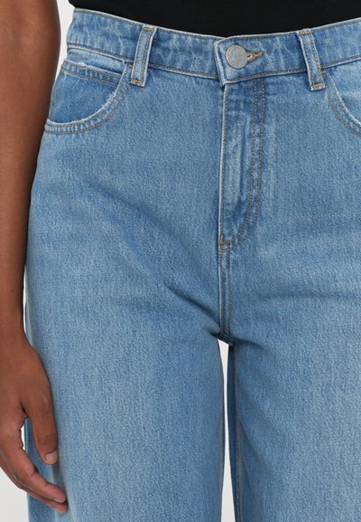 Hellblaue High-Waisted-Jeans mit strukturierter Denimhemdung, ausgestattet mit Vordertaschen, einem gebrandeten Knopf und genähten Nähten.