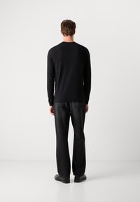 Schwarzes Langarmoberteil mit rundem Ausschnitt, kombiniert mit dunklen Denim-Hosen, von hinten betrachtet. Glatte Textur, schlichtes Design, einfarbig.