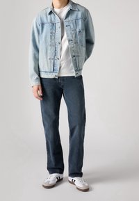 Ljusblå denimjacka med en framficka, vit t-shirt, mörkblå jeans och vita sneakers med grå och svarta detaljer.