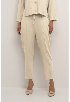 Bežový lněný outfit složený z krátkého hutného topu s knoflíky a zúžených kalhot se bočními švy, doplněný o světlé uzlové boty.