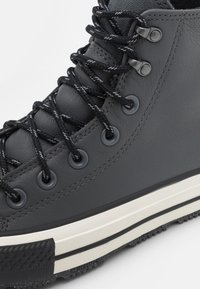 Zwarte leren hoge sneakers met zwarte veters, zilveren ogen en een witte rubberen zool met textuuraccenten.