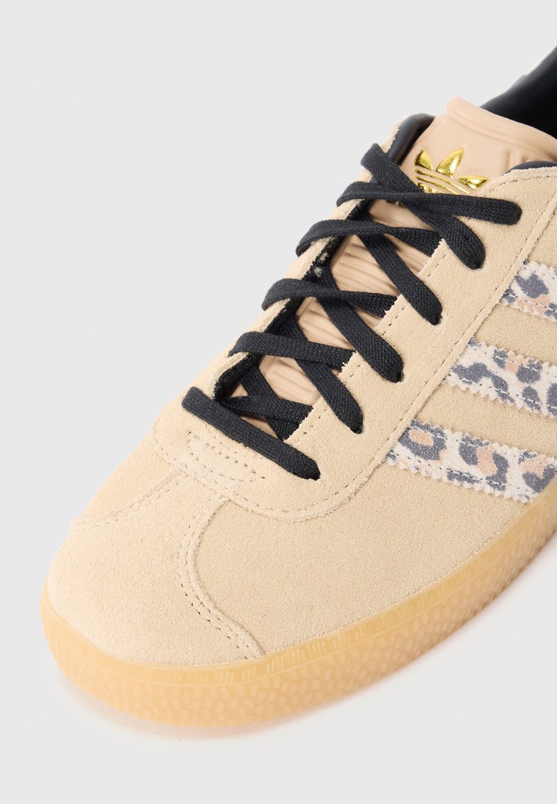 Beige Wildledersneaker mit schwarzen Schnürsenkeln, seitlich mit einem Leopardenmuster versehen. Gummisohle mit strukturiertem Finish. Goldene Logo-Akzent.