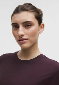 Burgundi värvi ümar kaelusega t-särk, mis on valmistatud pehmest kangast, sisaldades lihtsat disaini ja siledat tekstuuri, nähtavate õmblustega kaeluse ääres.