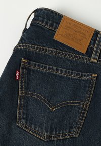 Poche arrière d'un jean Levi's bleu foncé avec surpiqûres jaunes, étiquette rouge Levi's et étiquette en cuir marron de la marque Levi Strauss & Co. à la ceinture.