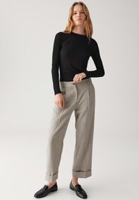 Top nero a maniche lunghe a coste abbinato a pantaloni larghi grigi con texture, caratterizzati da un risvolto, e mocassini neri. Design minimalista.