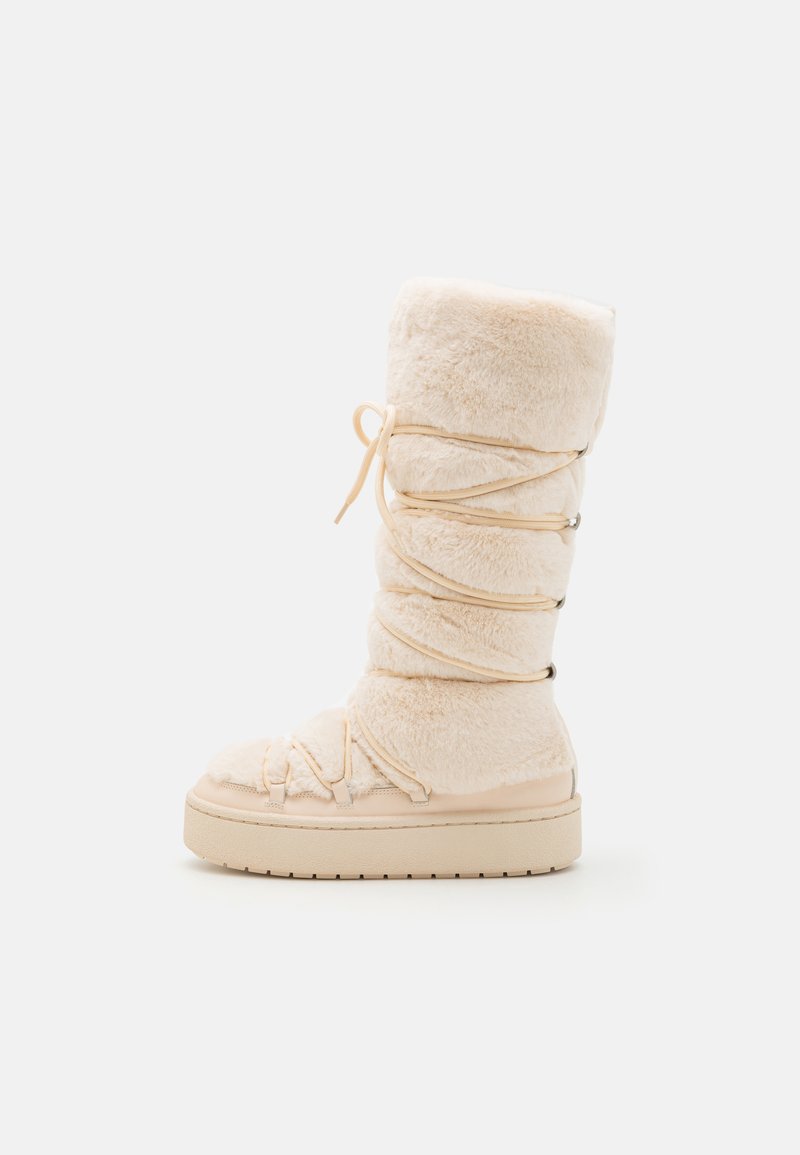 Lys beige knelengde støvel laget av mykt pelslignende materiale, med strukturert overdel, justerbar snøring og tykk såle.