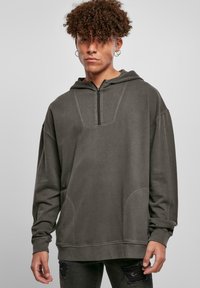 Mørk grå hettegenser med front glidelås, store lommer og raglanermer. Myk tekstur med subtile sømdetaljer.