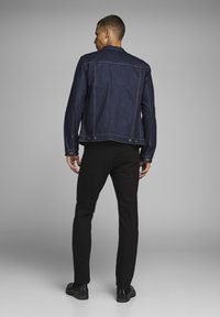 Tamno plavi traper jakna ravnog kroja, s minimalnim detaljima šivanja i dva gumba na rubu, u kombinaciji s crnim skinny hlačama.