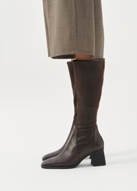 Stivali alti in pelle marrone con gambale aderente, punta quadrata e tacco a blocco, caratterizzati da una texture liscia e un design minimale.