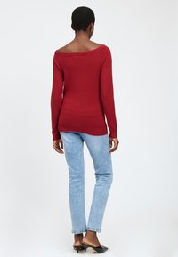 Maglione a collo scoperto rosso in maglia con maniche lunghe, design aderente e orlo a coste. Abbinato a jeans skinny azzurri chiari e mule nere con tacco.