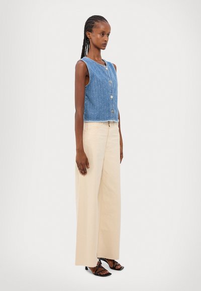 Denim vest in blue with front buttons, paired with high-waisted cream wide-leg pants and black strappy heeled sandals.