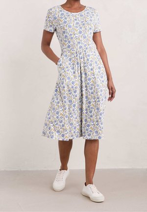 Bloemenprint jurk met korte mouwen in wit, blauw en geel, met een ronde halslijn en zijzakken, gecombineerd met witte sneakers.