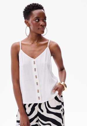 Witte linnen cami-top met verstelbare spaghettibandjes en een knoopsluiting aan de voorkant. Gepaard met zwart-witte zebraprint broek. Gouden creolen.