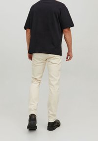 Svart bomullströja i avslappnad passform, tillsammans med ljusbeiga chinos. Skor i svart, slät läder. Enkelt design, inga synliga mönster.